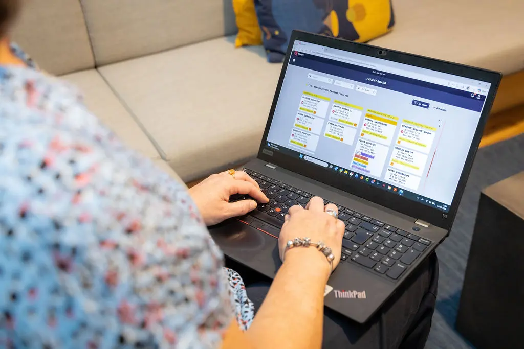 A clinician reviews a patient list via a kanban dashboard on a laptop.